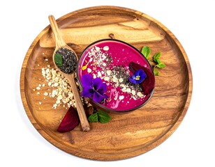 A vivid pink smoothie bowl with flowers and chia seeds on a wooden plate, top-down view against a white background