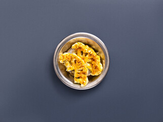 Crispy roasted cauliflower pieces are neatly arranged in a small metal bowl, showcasing their golden brown texture. This dish is perfect for sharing or for a healthy snack option at any meal.
