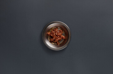 A metal bowl holds a generous serving of tender marinated meat, seasoned for flavor and arranged neatly on a dark surface, highlighting the dish's rich color and texture.