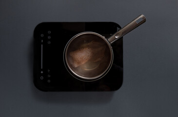 A stainless steel pot with simmering broth sits on a sleek electric stovetop. The scene captures a warm kitchen atmosphere, highlighting a cooking moment.