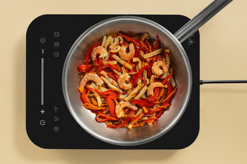 A vibrant mix of shrimp, red peppers, and onions sizzles in a silver skillet. The modern induction cooktop demonstrates efficient cooking in a bright kitchen setting.