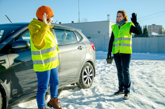 Volunteer road assistant in neon vest greeting older woman driver beside car on bright snowy day