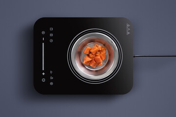 Raw meat chunks are placed in a stainless steel pot on a stylish induction cooktop. The modern kitchen features a clean, minimalist look with a smooth surface.