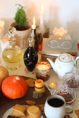 Lit candles, cookies, chocolate, nuts, tea, wine, pumpkins, books, reading glasses and autumn leaves on the table. Autumnal hygge at home. Selective focus.
