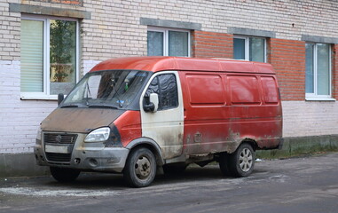 An old, rusty, multicolored minibus is parked near a brick wall, Prospekt Bolshevikov, Saint Petersburg, Russia, November 28, 2025