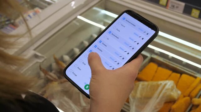 Hands of a contemporary consumer using a digital list while navigating store aisles. This relatable scene captures how technology integrates into daily shopping routines, excellent for supermarket