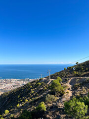 View from the mountain of the city at the foot and the dazzling blue sea on a clear day, cable car supports. Spain.