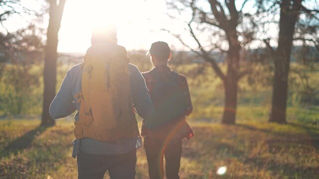 Silhouettes of men walking through forest with backpacks. Travel forest route with walking gear. Sunlight shining on outdoor adventure. Forest hiking backpack men walking through open trail.