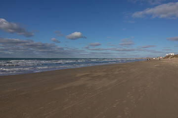View of the sea and clouds in winter. Waves on the sea turning into a blue sky with clouds. Winter sea during a storm. A sandy beach by the sea in the off-season.