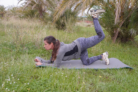 A woman doing gluteal exercises while balancing on one leg in a park