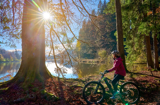 pretty woman riding her electric mountain bike at the pond of Hengelesweiher near city of Isny in the swabian  Allgaeu on warm autumn day, Bavaria, Germany