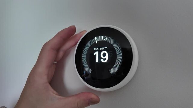 Person adjusting smart thermostat to reduce energy use and enhance comfort