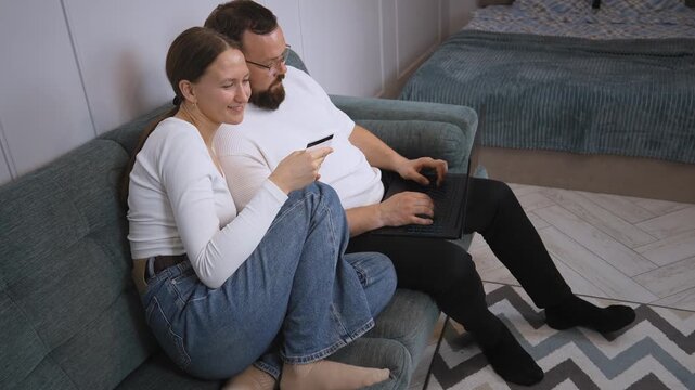 Young couple sitting on couch and using world wide web for home shopping and using credit card and laptop to shop online