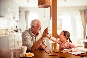 Happy senior grandfather and child granddaughter high-fiving over homework at home