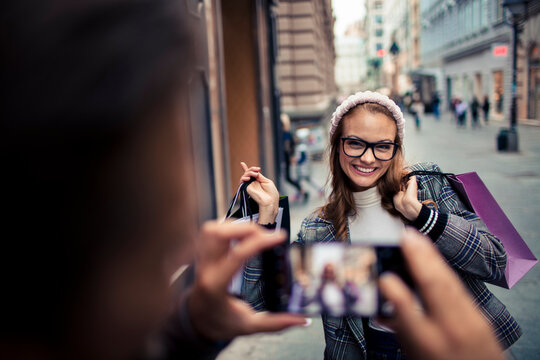 Young adult woman happily posing for smartphone photo downtown with shopping bags