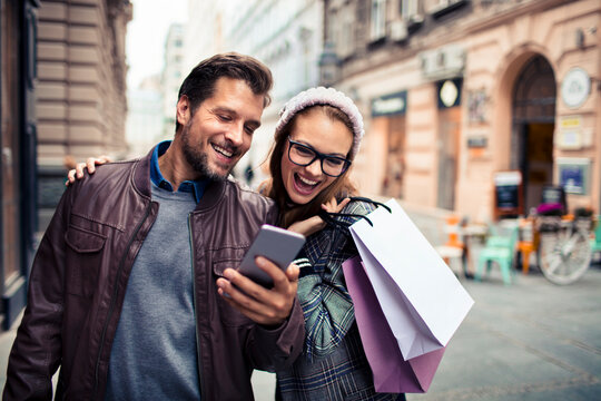 Adult couple laughing at smartphone while shopping on city street