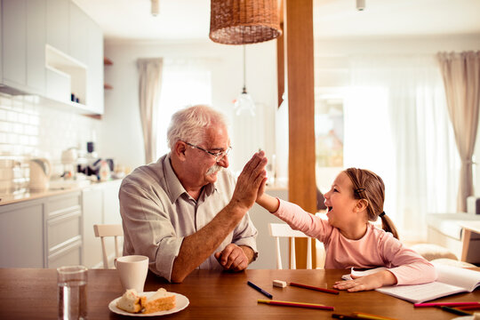 Happy senior grandfather and child granddaughter high-fiving over homework at home