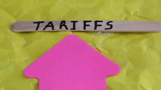 Un primer plano de una paleta de madera con la palabra de aranceles y una flecha de color rosado con movimiento en un fondo amarillo. Pol&iacute;tica econ&oacute;mica 