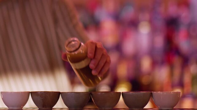 Preparing liquor. Asian pub. Male bartender filling portioned small ceramic cups for sake. Man serving traditional japanese alcoholic order.