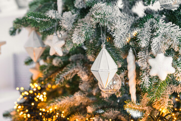 Snowy frosted Christmas tree branches decorated with white ornaments, warm glowing string garland lights, illumination on background. Soft winter atmosphere for holiday backdrop and seasonal designs