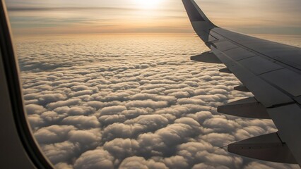 Airplane wing view above fluffy clouds during golden hour at sunset