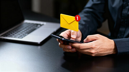 Person checking email notification on smartphone with laptop in background