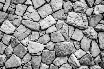 Fototapeta premium Close up textured grayscale image of a natural stone wall with irregular shapes and rough surfaces