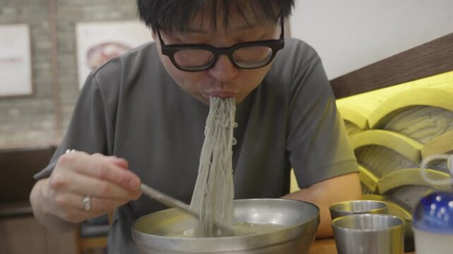 Asian man slurping cold noodles in restaurant &ndash; close-up eating Korean soba