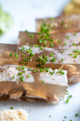 Detailed view of aspic slices garnished with chopped green herbs on a plate highlighting texture and garnish.