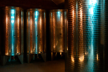 Artisanal winery equipment. Gleaming stainless steel fermentation tanks within a dimly lit industrial space, accented with colorful light reflections.