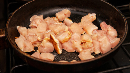 raw chopped chicken being sauteed in a frying pan