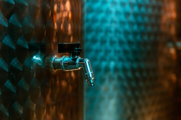 Artisanal winery equipment. Gleaming stainless steel fermentation tanks within a dimly lit industrial space, accented with colorful light reflections.