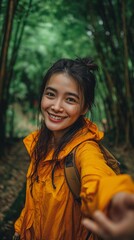A pleasant young woman wearing an orange jacket is shown in this image of a bamboo forest hand stretching toward the camera while grinning.