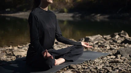 Fotobehang Lotusbloem Person meditating outdoors in lotus position on rocky riverside  © Mariia