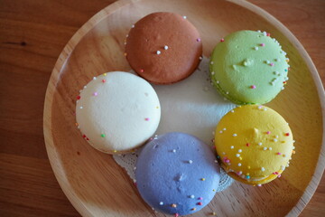 カラフルなマカロンを木皿に5個配置した俯瞰写真。パステルカラーと可愛い装飾が映えるスイーツイメージで、カフェ・メニュー・広告・SNS風ビジュアルに最適