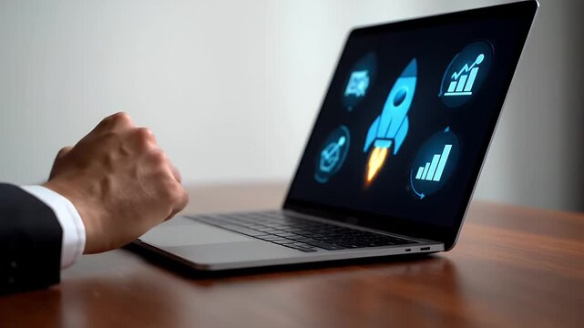 Hand Typing on Laptop Showing Rocket Startup Illustration on Screen in Office Setting on Wooden Desk in Dark Suit Jacket with Blurred White Wall Background