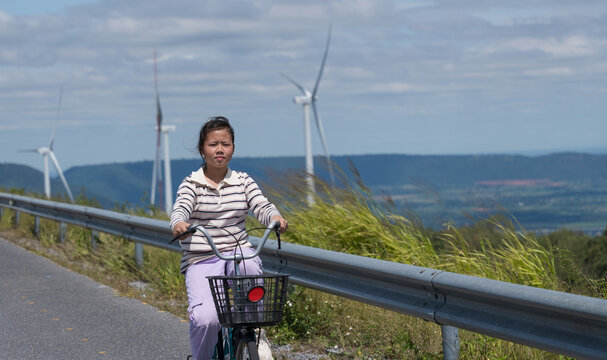 Young girl cycling on countryside road with wind turbines, eco-friendly lifestyle and clean energy.