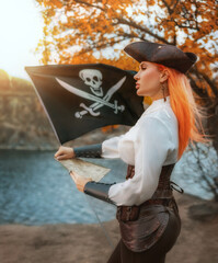 Art photo real person fantasy woman captain pirate holding in hands map searching for treasure looking for wealth. Fairy tale girl thief game old style costume. black pirate flag fly flutters in wind