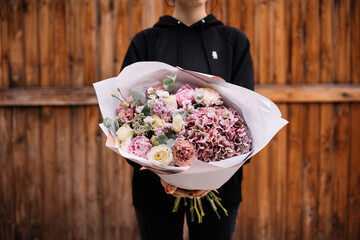 Very nice young woman holding big and beautiful bouquet of fresh hydrangea, roses, carnations, eustoma, eucalyptus flowers in pastel pink and yellow colors
