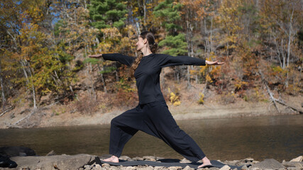 Woman practicing yoga outdoors in Warrior II pose by a lake in autumn