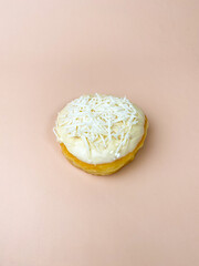 Coconut-topped donut with white frosting on soft pink background for food photography