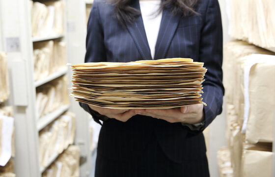 保管庫でファイリングされたたくさんの紙の書類と、女性スタッフの手元　顔無し