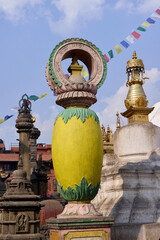 A vibrant stupa ornament stands tall against a clear blue sky at Swayambhunath, a UNESCO World Heritage Site in Kathmandu. Surrounding prayer flags flutter in the breeze