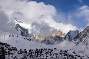 Snow covered mountains peak through the clouds near Annapurna Base Camp in the Himalayas, Nepal. Sunlight illuminates some of the peaks, creating a dramatic effect.
