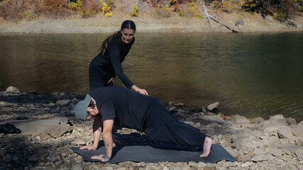 Outdoor yoga session with instructor helping student by riverside