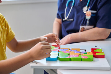 Child engages in playful puzzle activity with healthcare worker in a bright clinic during afternoon...