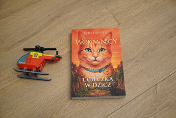 Naklejka premium Polish edition of Warriors: Into the Wild book with a toy helicopter on wooden floor