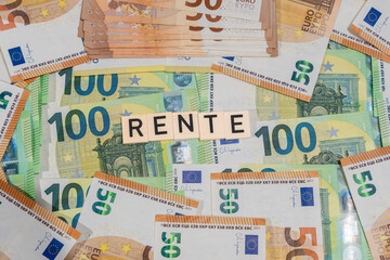 The word Rente in wooden tiles sits on a collage of euro notes. Concept for pension systems, retirement funding, and personal finances.