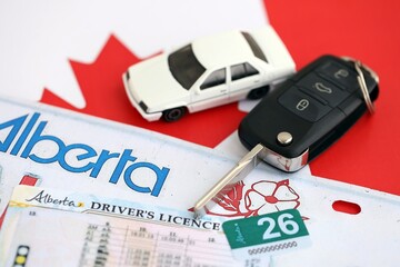 Alberta canadian car license plate and ignition key on flag of Canada close up. Driving permit and registration concept
