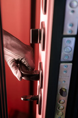 Hand in black leather glove opening armored door handle from inside with red light. Concept of...
